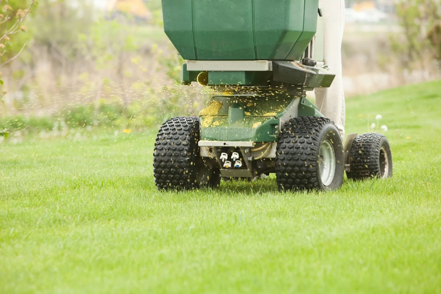 A broadcast spreader applying lawn care material across green turf.